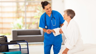 Junge Pflegerin hilft Seniorin beim Aufstehen