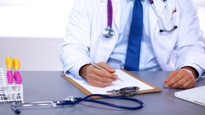 Arzt an seinem Schreibtisch arbeitet mit medizinischen Geräten im Hintergrund 