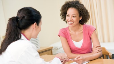 Eine Ärztin zeigt und erklärt einer Patientin lächelnd einen Zettel. Die Patinetin lächelt auch.