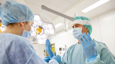 In einem Operationssaal werden dem Chirurg die Handschuhe angezogen, er hält dabei die Hände hoch.