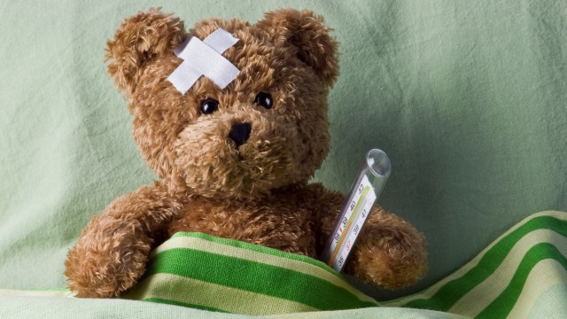 Kranker Teddy mit Fieberthermometer im Bett