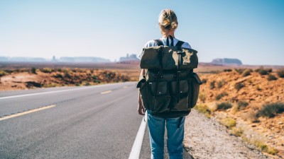  Rückansicht einer Reisenden in T-Shirt und Jeans mit Rucksack am Straßenrand der historischen Route in den Vereinigten Staaten